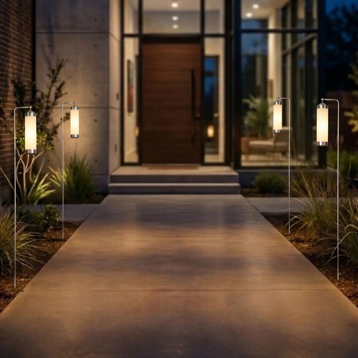 Vier chromfarbene Gartenlaternen mit gefrostetem Glas entlang eines beleuchteten Eingangsweg vor dem Haus
