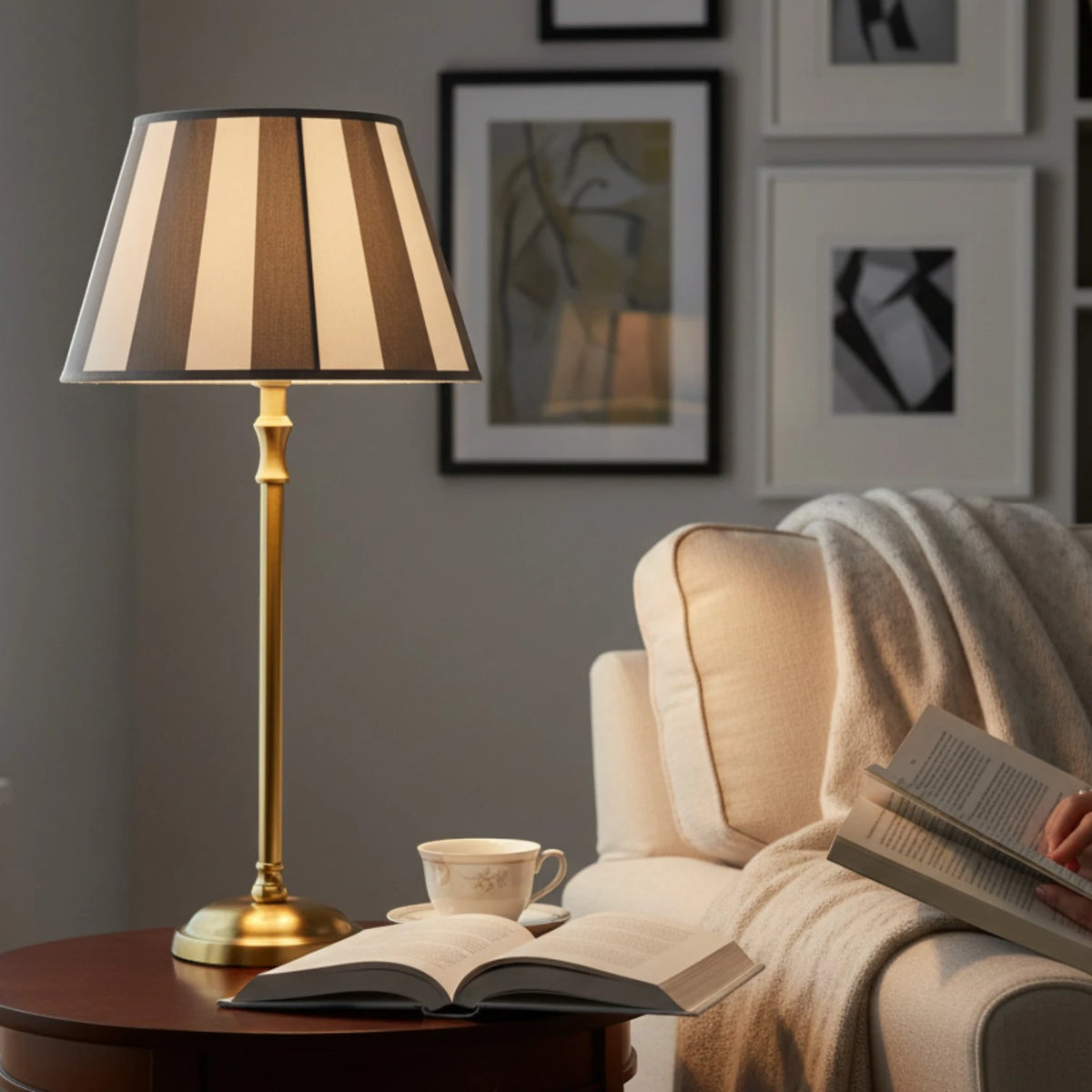 Lampenschirm in Taupe und Weiß gestreift auf einer Tischlampe mit schlankem goldfarbenem Fuß auf einem Holztisch im Wohzimmer.