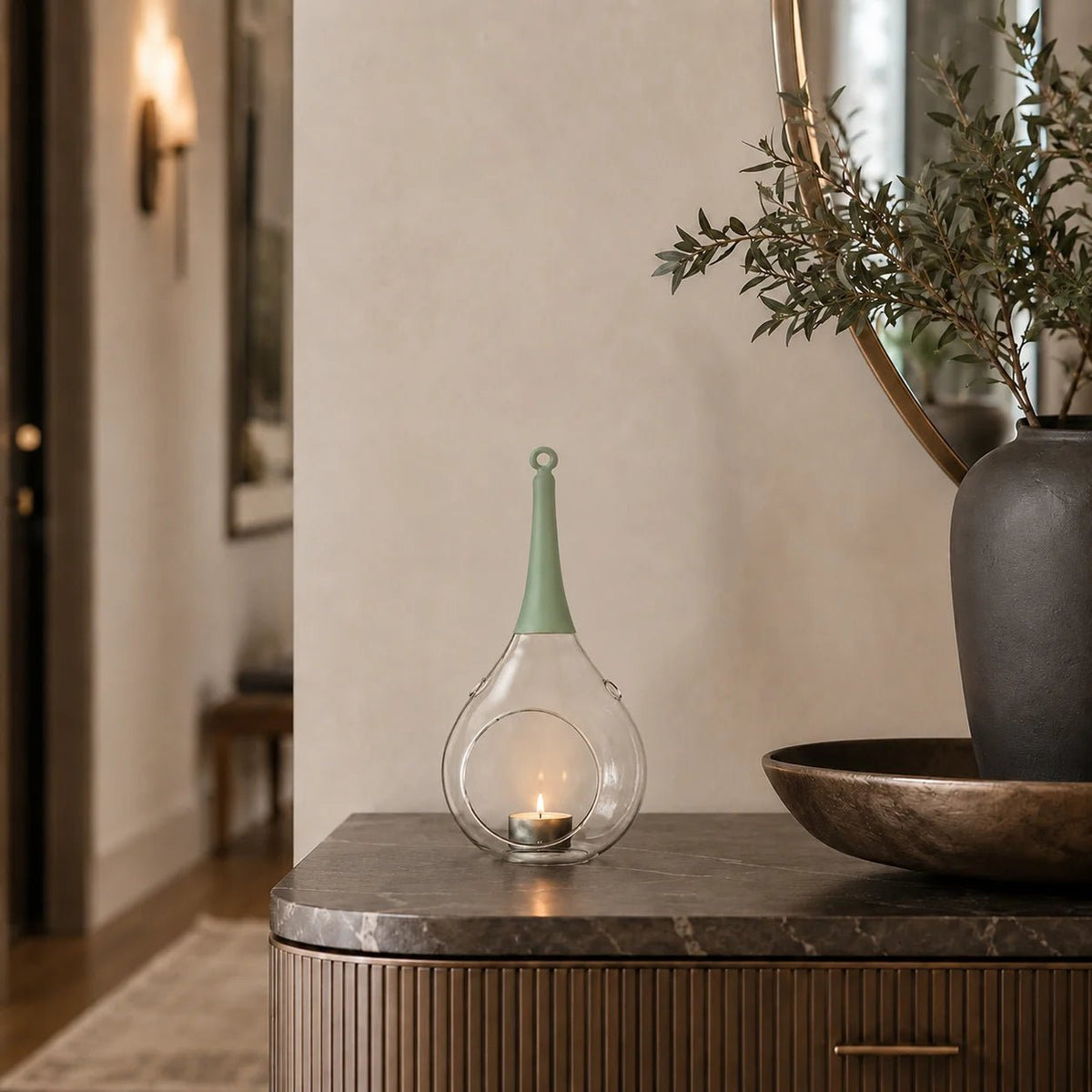 ompex Taura Windlicht in Grün aus Glas mit brennendem Teelicht auf einer modernen Kommode im Flur